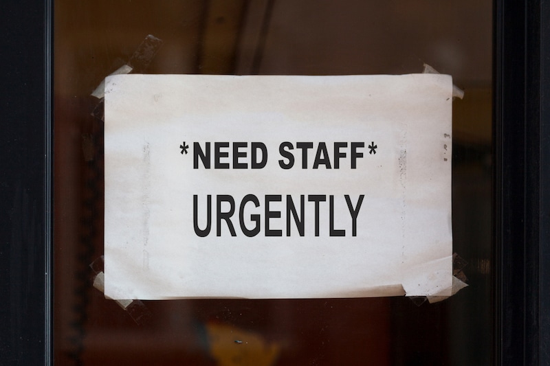 "NEED STAFF* URGENTLY sign taped to window.