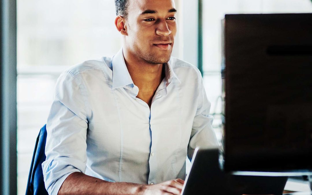 Man sits at his desk looking at laptop.