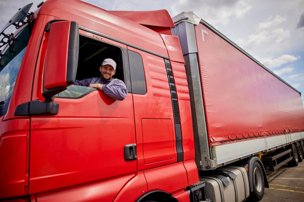 Truck driver smiling out the window of a red truck.