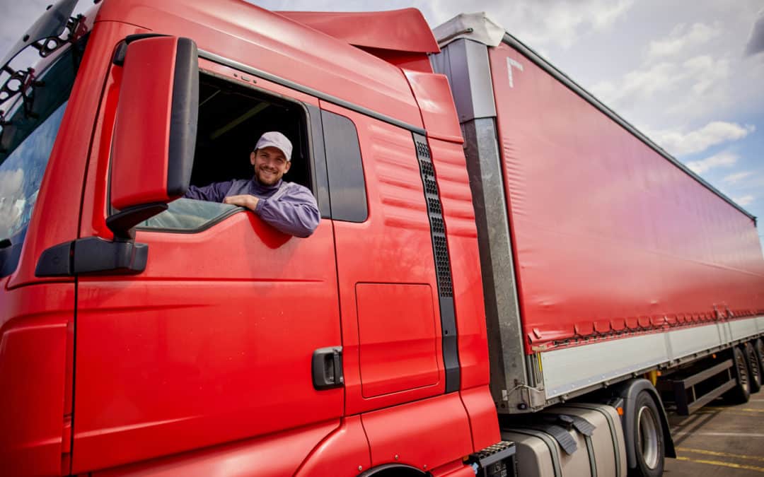 Truck driver smiling out the window of a red truck.